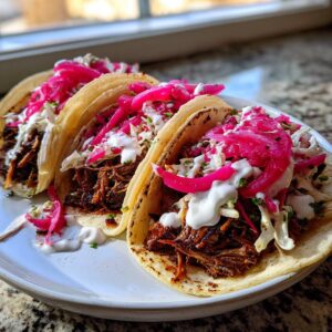 Three fully loaded Hanukkah brisket tacos featuring shredded meat, slaw, bright pink pickled onions, and crema.