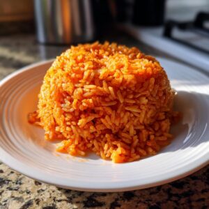 A perfectly molded mound of bright orange Kwanzaa Jollof rice served on a white plate.