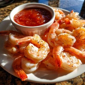 A plate of classic shrimp cocktail, featuring plump, cooked shrimp seasoned with pepper, served with a side of cocktail sauce.