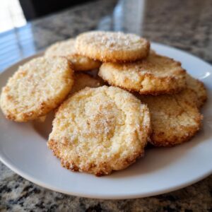 A pile of golden brown sugar cookies, generously sprinkled with sparkling sugar, on a white plate.
