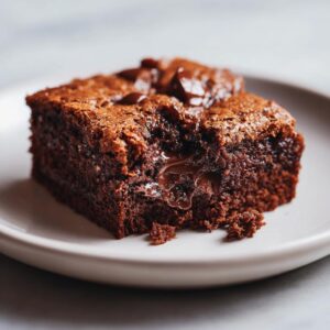 A close-up of a rich, dark vegan brownie slice with gooey, melted chocolate chips and a fudgy center.