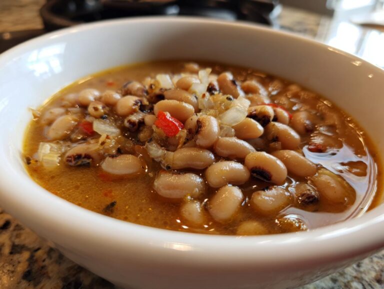 Close-up of a white bowl filled with a savory black eyed peas recipe, garnished with onions and red pepper.