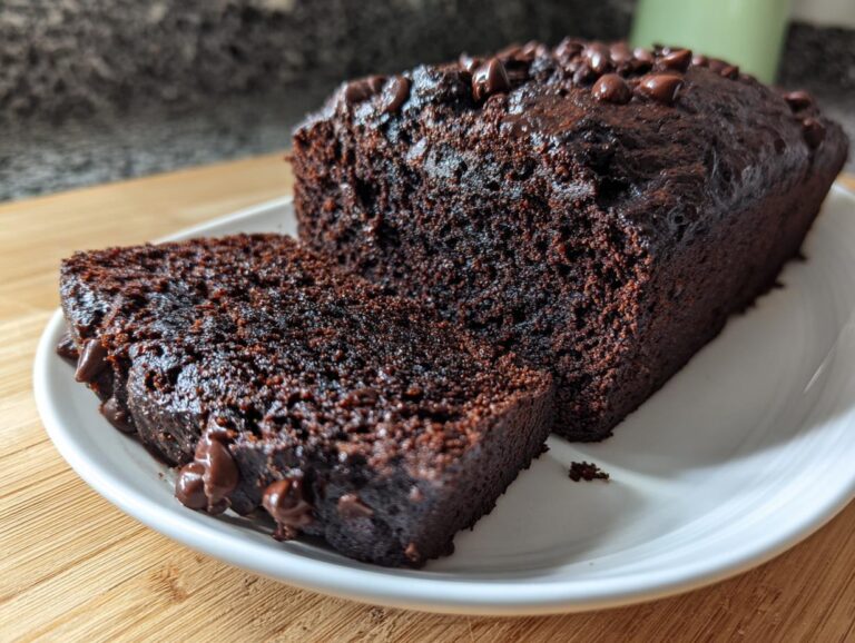 A slice cut from a rich, dark chocolate banana bread loaf topped with melted chocolate chips.