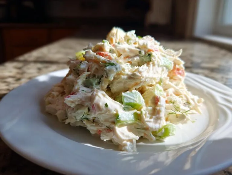 A generous scoop of creamy crab salad with visible chunks of celery and herbs on a white plate.