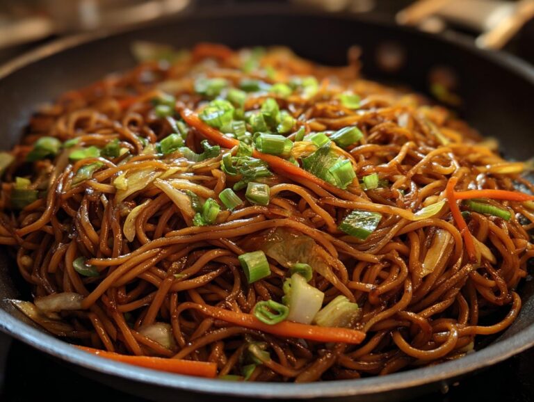 A close-up shot of glossy, dark brown fried noodles mixed with shredded carrots and cabbage, topped with fresh green onions.