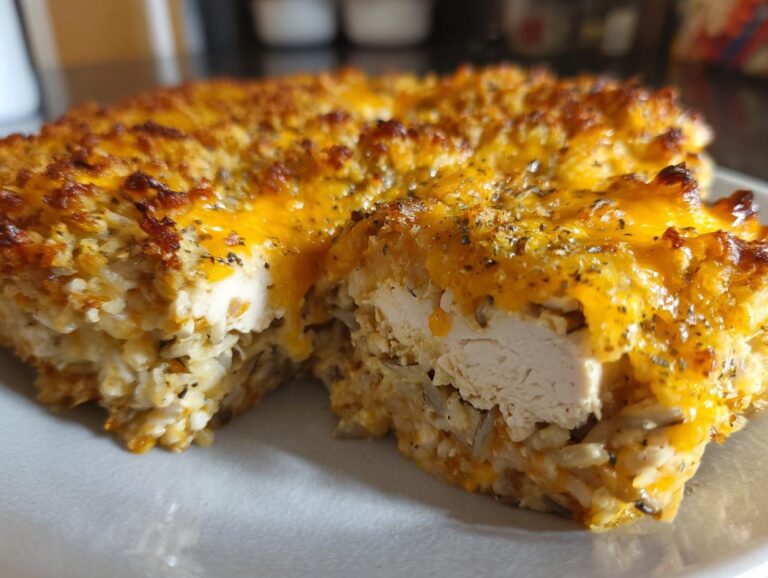 A close-up of a baked chicken and wild rice casserole slice showing tender chicken breast surrounded by creamy rice and topped with melted cheddar cheese.