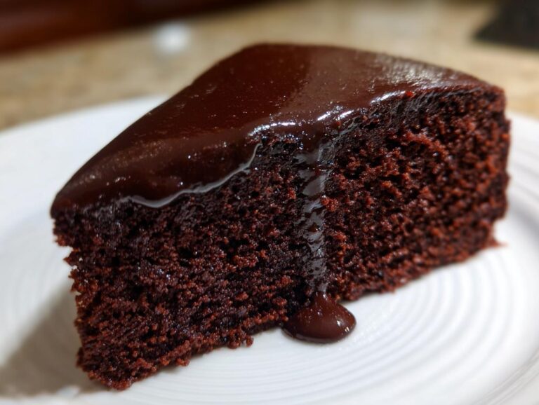 Close-up of a moist slice of flourless chocolate cake topped with dripping dark chocolate ganache.