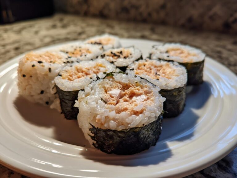 Close-up of several slices of spicy tuna kimbap, featuring rice, nori, and a creamy tuna filling, sprinkled with sesame seeds.