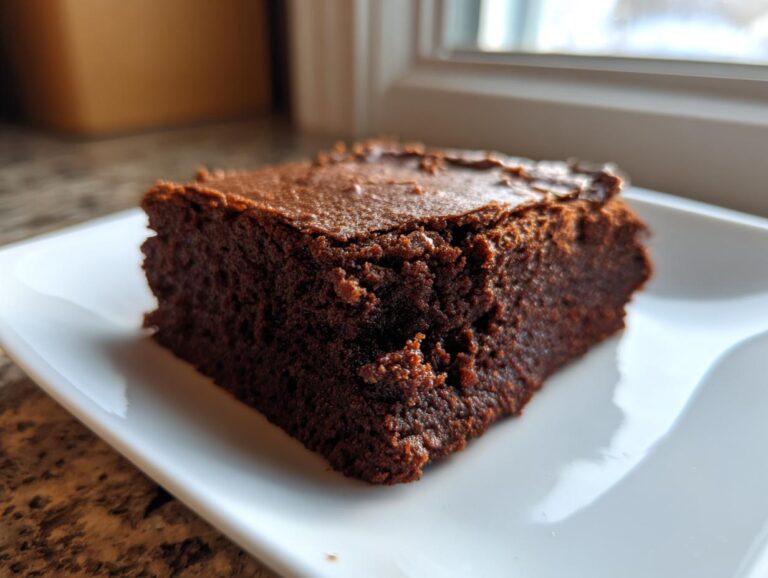 A close-up of a single, rich, dark slice of chewy gingerbread brownies resting on a white rectangular plate.
