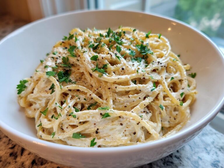 A close-up of creamy parmesan pasta tossed in a white bowl, topped with fresh parsley and black pepper.