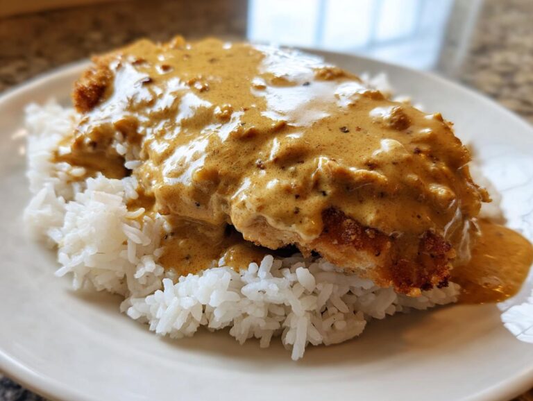 Close-up of a breaded chicken breast smothered in creamy brown gravy served over white rice, featuring the smothered chicken and rice dish.