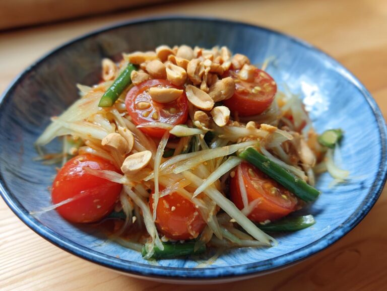 Close-up of a vibrant papaya salad topped with crushed peanuts, cherry tomatoes, and green beans.