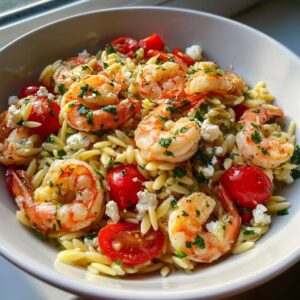 A close-up view of a bowl filled with amazing shrimp orzo salad featuring plump shrimp, cherry tomatoes, and feta cheese.