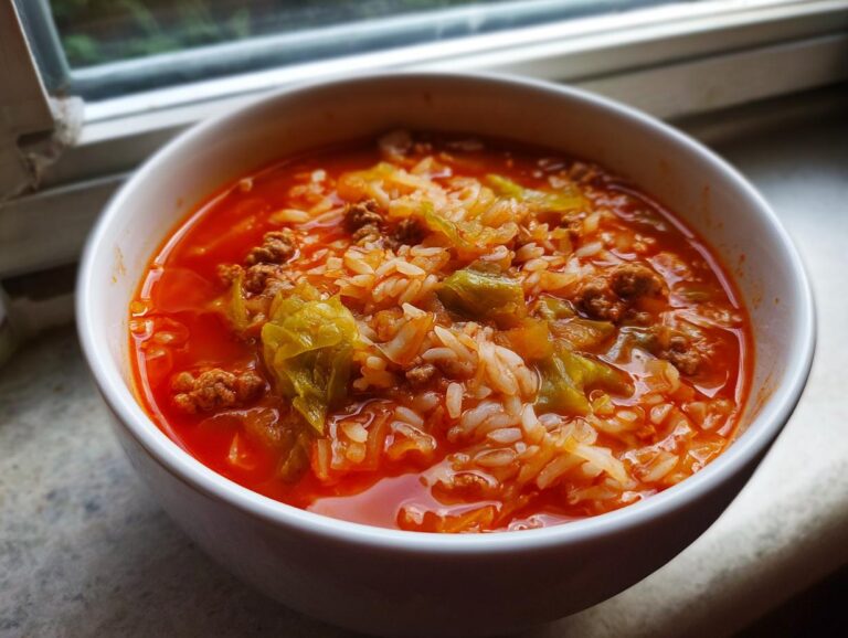 Close-up of a white bowl filled with rich, red Golumpki soup containing ground meat, rice, and cabbage.